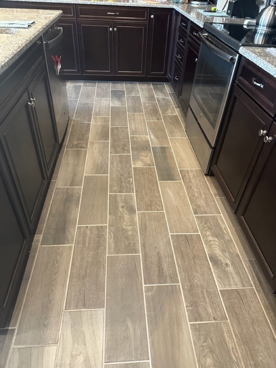 A clean wood-look tile kitchen floor between dark cabinets