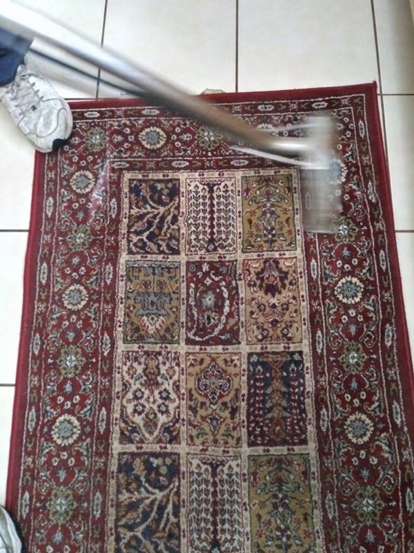 A red patterned rug being cleaned on a tile floor
